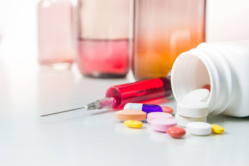 Red liquid in disposable syringe with pills and bottles.