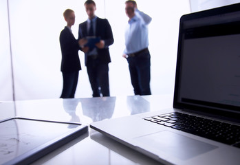 Laptop  computer on  desk , three businesspeople standing in the