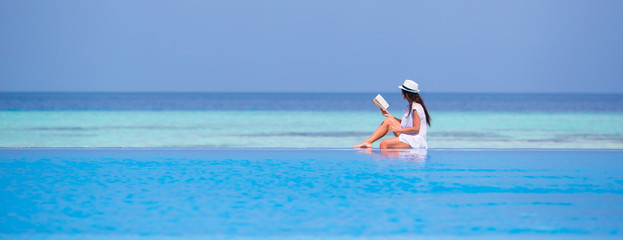 Young girl reading book near swimming pool