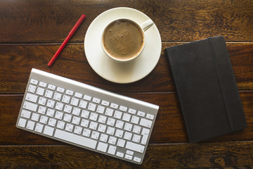 Keyboard, pencil, black notebook and a cup of coffee.