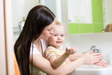 mother teaches kid washing hands in bathroom