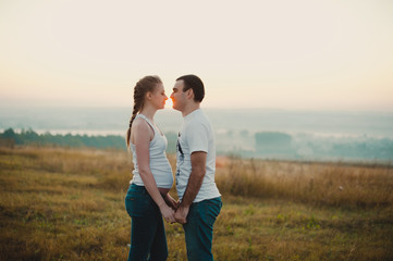 Fototapeta na wymiar Young pregnant couple holding hands and standing in a field 