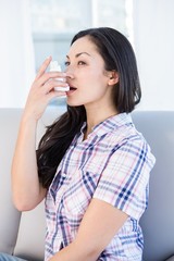 Pretty brunette using inhaler on couch