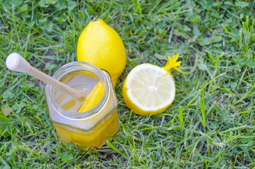 Jar of honey, dipper, lemon and yellow flowers in the grass