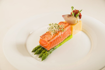 A piece of fried salmon, asparagus and corn porridge on a white