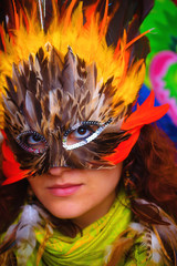 Young woman with a colorful feather carnival face mask on bright