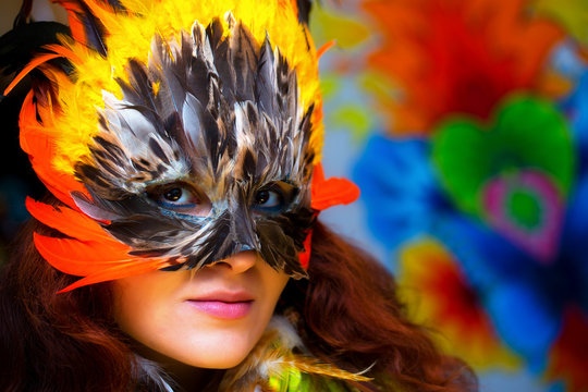 Young woman with a colorful feather carnival face mask on bright