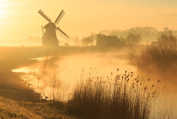 Moulin à vent pendant un lever de soleil brumeux et jaune dans la campagne.