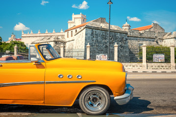 Vintage car parked next to an old castle in Havana