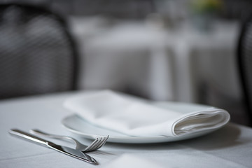 Close up of knife, fork, plate and folded napkin upon table
