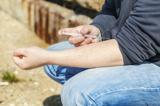 Drug addict man with syringe in hand near wall