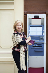 Mature blonde woman with credit card in hand near ATM