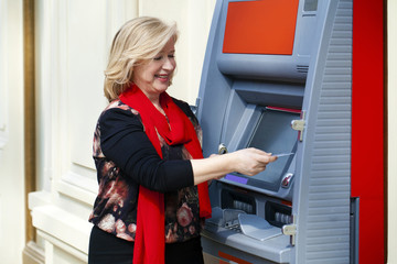 Fototapeta na wymiar Mature blonde woman with credit card in hand near ATM