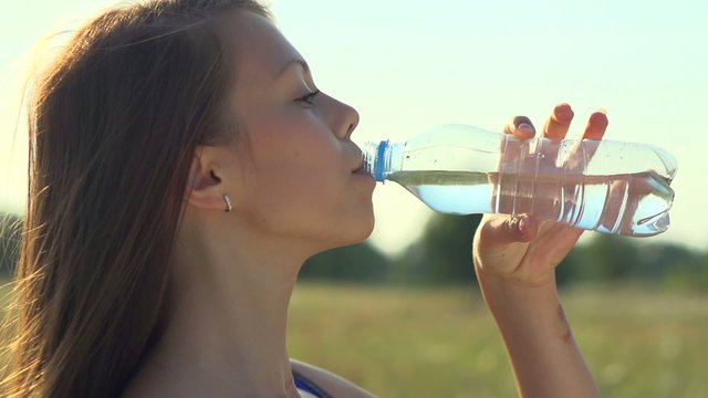 Healthy teen girl drinking water from the bottle outdoors