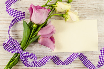 Empty postcard, flower and purple ribbon on wooden background