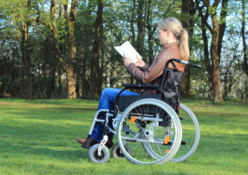 Frau im Rollstuhl liest Buch im Park.JPG