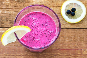 Blueberry smoothie in a glass with a peace of lemon, over vintag