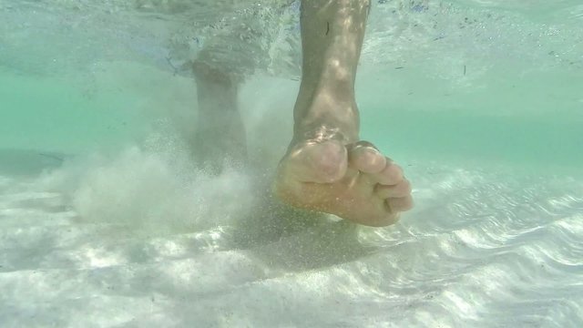 Closeup underwater barefeet walking over shallow sandy sea floor