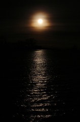 Dark high contrast shot of misty sun with reflections on the water