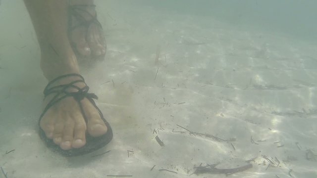 Closeup underwater walking over sandy shoal in sandals