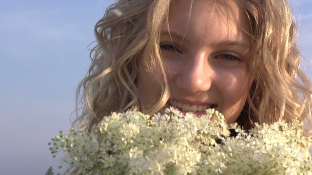 Beauty happy girl with curly blond hair smelling wild flowers