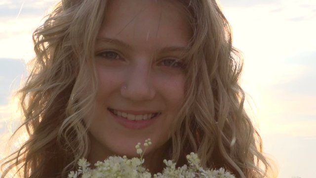 Beauty happy girl with curly blond hair smelling wild flowers