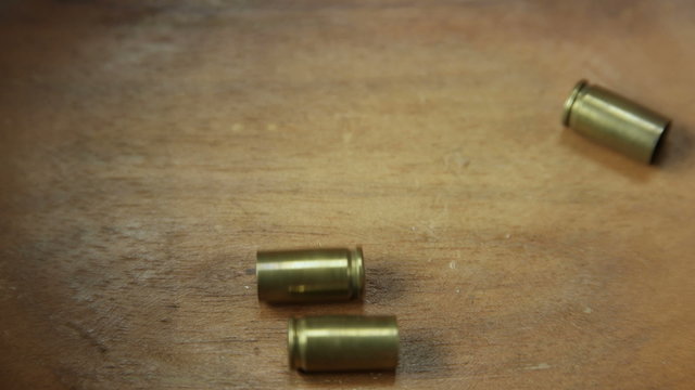 Three bullet casings falling onto wooden BG center frame 4K UHD