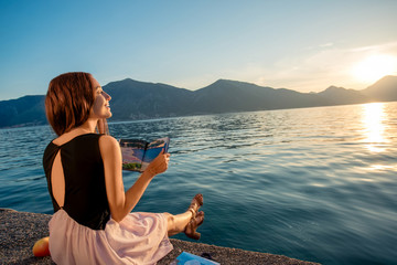 Fototapeta premium Young woman sitting on the pier at sunrise