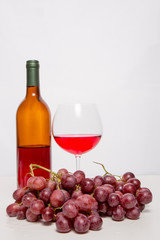 Glass of red wine and red grapes on white background