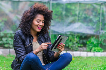 exotic beautiful young girl sitting in the garden using tablet