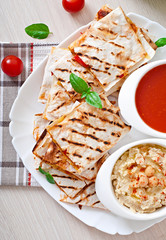 Mexican Quesadilla sliced with vegetables and sauces on the tabl