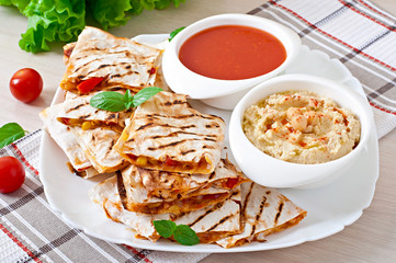 Mexican Quesadilla sliced with vegetables and sauces on the tabl