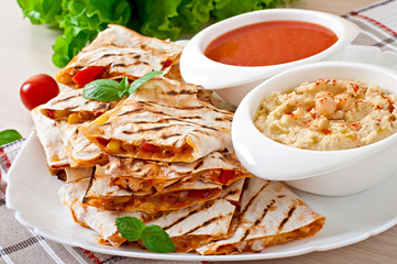 Mexican Quesadilla sliced with vegetables and sauces on the tabl