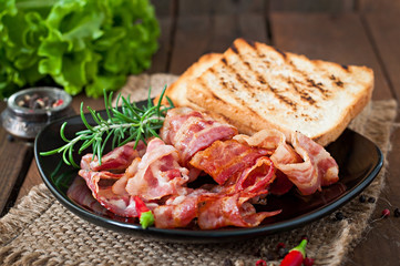 Fried bacon and toast on a black plate on a wooden background