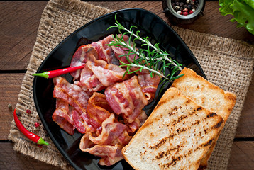 Fried bacon and toast on a black plate on a wooden background