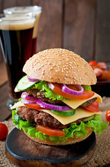 Big juicy hamburger with vegetables and beef on a wooden table