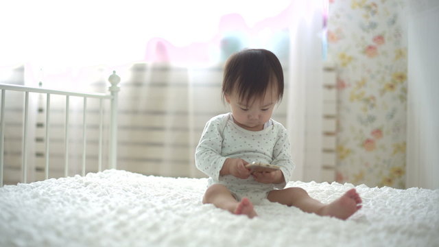 little asian baby sitting and playing with smartphone