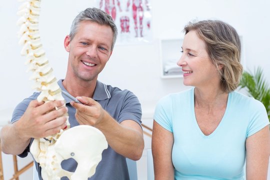 Physiotherapist showing spine model to his patient - Powered by Adobe