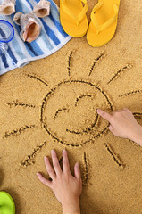 Smiling sun happy smiley face drawing drawn in sand with child hands on a tropical beach with seashells and accessories summer holiday vacation photo vertical
