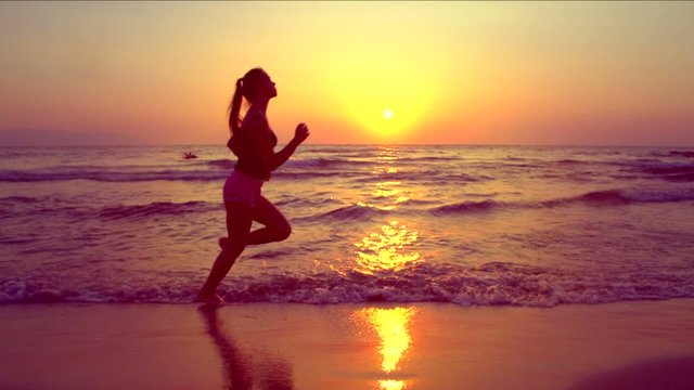 Beauty girl jogging along the sea coast over sunset