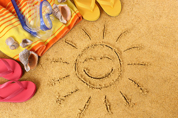 Fototapeta na wymiar Smiling sun happy smiley face drawing drawn in sand with child hands on a tropical beach with seashells and accessories summer holiday vacation photo