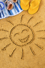 Smiling sun happy smiley face drawing drawn in sand with child hands on a tropical beach with seashells and accessories summer holiday vacation photo vertical