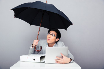 Businessman sitting at the table with laptop and holding umbrell