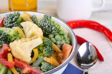 Frozen vegetables in bowl on napkin, on wooden table background
