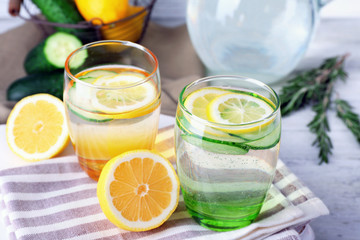 Fresh water with lemon and cucumber in glassware on wooden table, closeup
