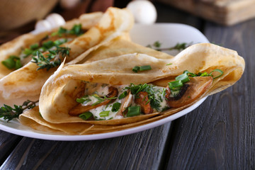 Pancakes with creamy mushrooms in plate on wooden table,