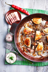Fried dumplings with onion and bacon in frying pan,