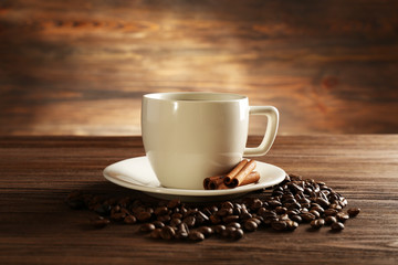 Cup of coffee with grains and cinnamon sticks on wooden background