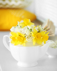 Beautiful bouquet of yellow daffodils and roses in teapot on windowsill