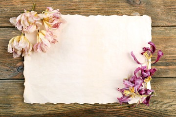 Dried flowers on sheet of paper on wooden table, top view
